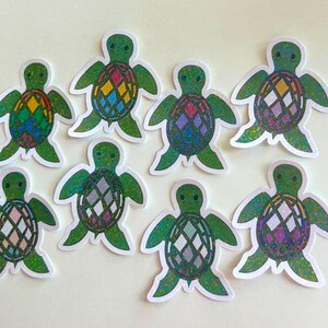 May include: Eight green turtle stickers with iridescent glitter. Each turtle has a different colored geometric pattern on its shell.