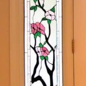 May include: A stained glass sidelight featuring a stylized branch with pink flowers and green leaves. The sidelight is 12.5 inches wide and 78 inches tall. The text "Dogwood Sidelight 12.5x78 (was $1595) now $650" is displayed above the sidelight.