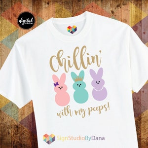 May include: White t-shirt with the text "Chillin' with my peeps!" in gold lettering. Three pastel-coloured Peeps marshmallow bunnies are pictured below the text. The text "SignStudioByDana" is at the bottom of the shirt.