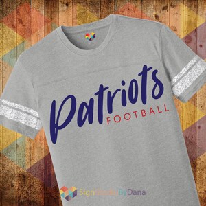 May include: Gray t-shirt with white stripes on the sleeves and the words "Patriots Football" in blue and red lettering.