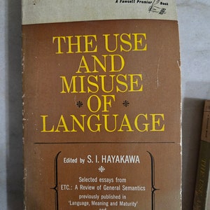 May include: Vintage paperback book titled "THE USE AND MISUSE OF LANGUAGE" by S. I. Hayakawa. The cover is brown with yellow lettering and a cream-colored top section. The book is a Fawcett Premier Book.