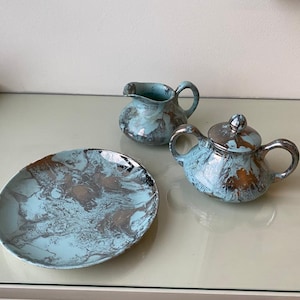 May include: A teal blue and silver creamer, sugar bowl, and plate with a marbled design.
