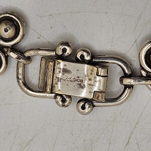 Puede incluir: Primer plano de un cierre de joyer&iacute;a plateado con el nombre de la marca "Brighton" grabado. El cierre est&aacute; conectado a una cadena con eslabones circulares decorativos.
