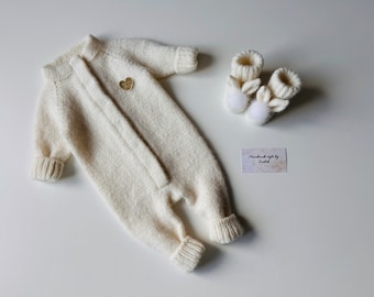 Puede incluir: Un pelele blanco de punto para bebé con un charm de corazón dorado y zapatillas de punto de conejo blanco a juego con pompones. Estilo hecho a mano por Judith.