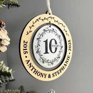 May include: A round wooden and silver ornament with the text "2015 - Anthony & Stephanie - 2025" and a silver circle with the text "10 Years" inside a wreath design.