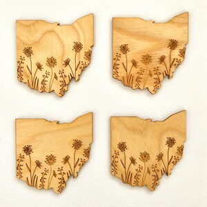 Puede incluir: Cuatro posavasos de madera con forma del estado de Ohio con un dise&ntilde;o de flores silvestres grabado con l&aacute;ser. Los posavasos son de madera marr&oacute;n claro y tienen un acabado natural.