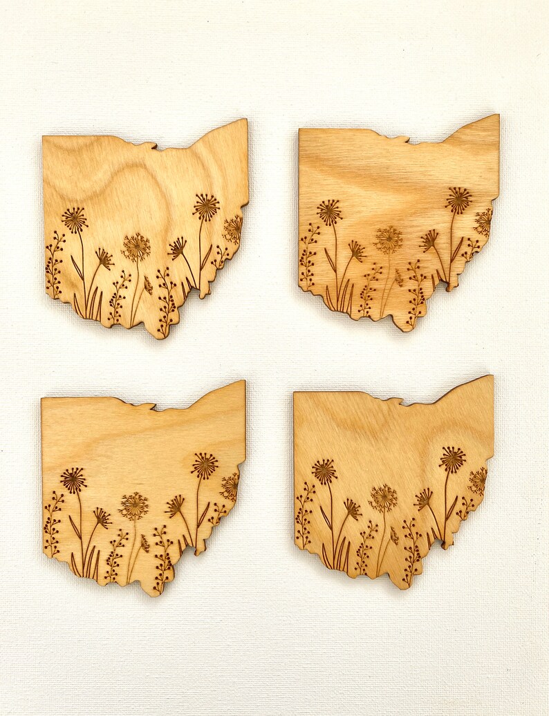 Puede incluir: Cuatro posavasos de madera con forma del estado de Ohio con un dise&ntilde;o de flores silvestres grabado con l&aacute;ser. Los posavasos son de madera marr&oacute;n claro y tienen un acabado natural.