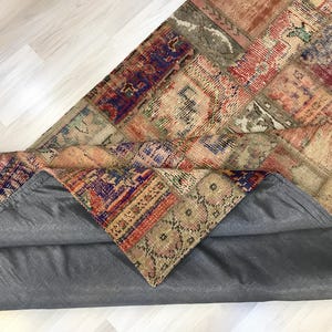 Puede incluir: Una alfombra de patchwork multicolor con respaldo gris. La alfombra presenta una variedad de patrones y colores, incluyendo rojo, azul y beige. La alfombra est&aacute; parcialmente enrollada, revelando el respaldo gris.