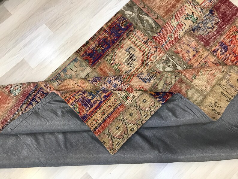 Puede incluir: Una alfombra de patchwork multicolor con respaldo gris. La alfombra presenta una variedad de patrones y colores, incluyendo rojo, azul y beige. La alfombra est&aacute; parcialmente enrollada, revelando el respaldo gris.