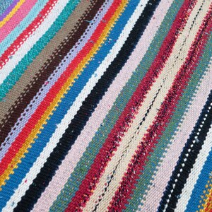 May include: A colorful striped rug with a variety of colors, including red, blue, green, yellow, and white. The rug is woven with a simple pattern and has a slightly textured surface.