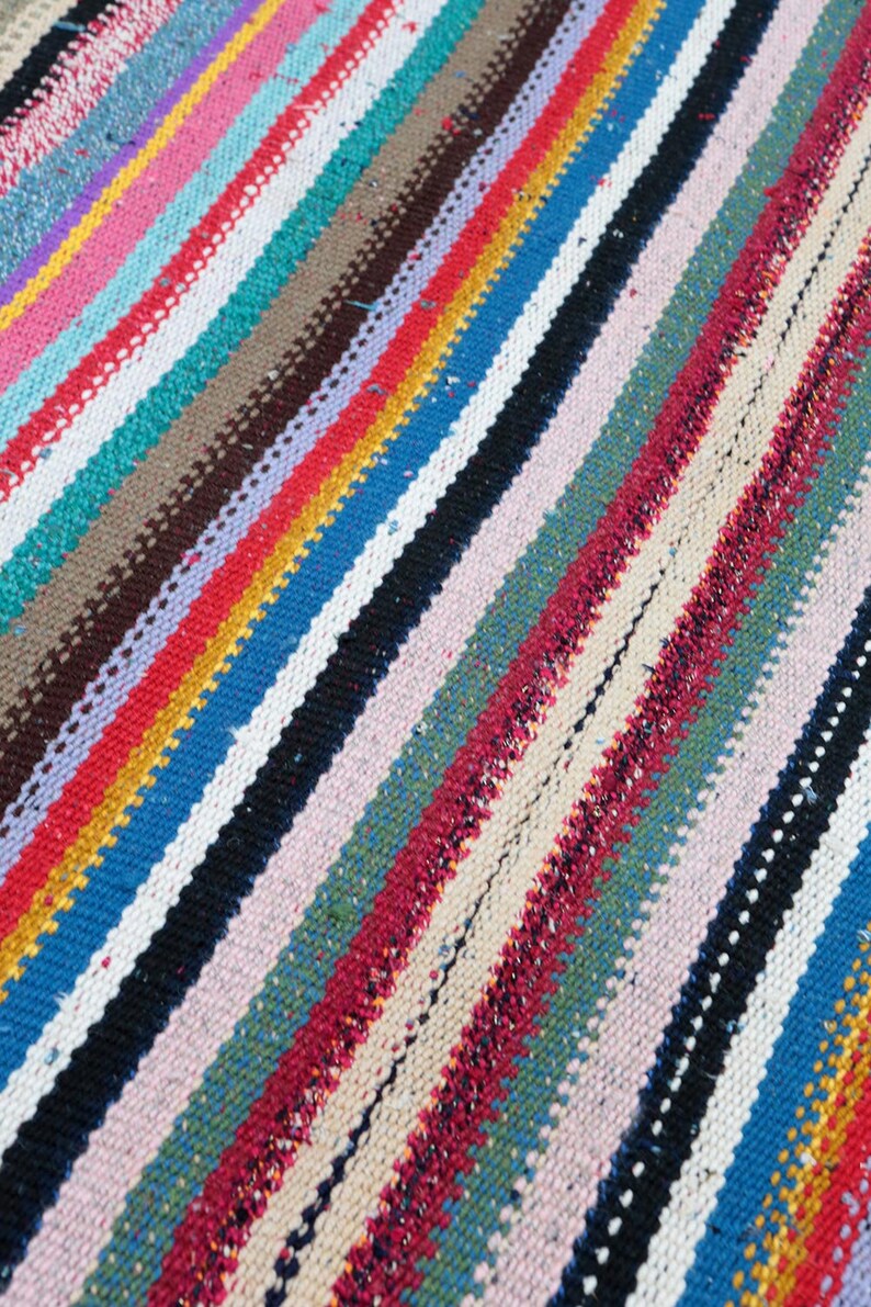 May include: A colorful striped rug with a variety of colors, including red, blue, green, yellow, and white. The rug is woven with a simple pattern and has a slightly textured surface.