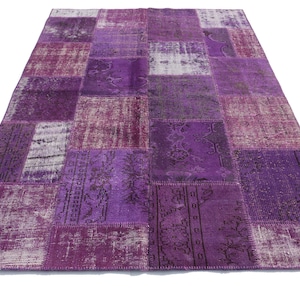 Könnte beinhalten: Ein Patchwork-Teppich in Lila- und Weißtönen. Der Teppich besteht aus verschiedenen Stoffstücken, die zusammengenäht wurden.