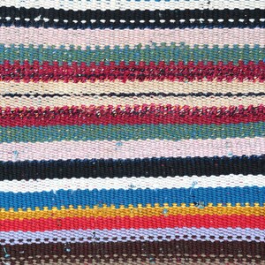 May include: A colorful woven rug with stripes of red, blue, yellow, green, white, and brown. The rug is made of a thick, textured fabric.