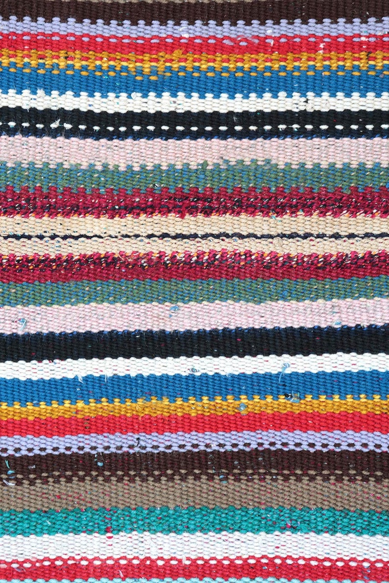 May include: A colorful woven rug with stripes of red, blue, yellow, green, white, and brown. The rug is made of a thick, textured fabric.