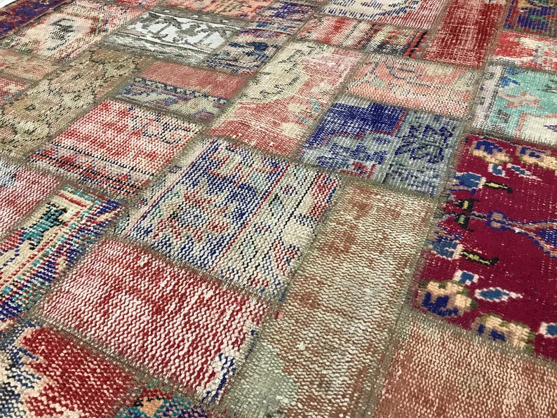 Puede incluir: Primer plano de una alfombra patchwork con una variedad de colores y patrones. La alfombra presenta parches rectangulares y cuadrados en tonos de rojo, azul, beige y crema. El dise&ntilde;o tiene un aspecto vintage y desgastado.