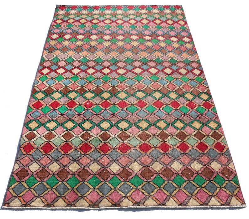 May include: A vintage rug with a geometric pattern of colorful diamonds in shades of pink, red, green, blue, and brown. The rug has a faded, distressed look, giving it a unique and antique feel.