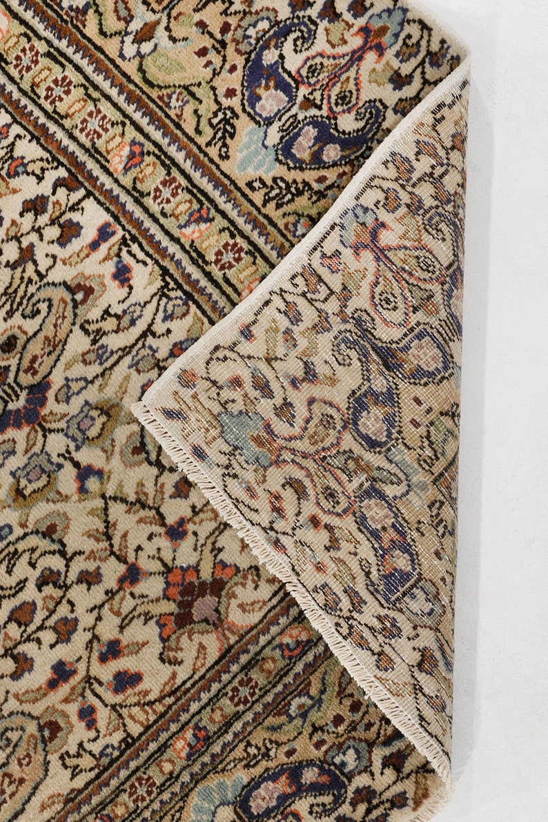 K&ouml;nnte beinhalten: Nahaufnahme der R&uuml;ckseite eines beigen Teppichs mit einem detaillierten Blumenmuster in Braun-, Blau- und Rott&ouml;nen. Der Teppich hat einen Fransenrand.