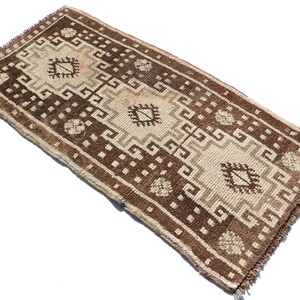 May include: A brown and cream patterned rug with a geometric design. The rug has a fringed edge.
