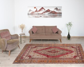 Puede incluir: Una alfombra vintage con un patrón geométrico rojo, crema y marrón. La alfombra está colocada sobre un suelo de madera clara en un salón con un sofá y un sillón.
