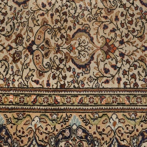K&ouml;nnte beinhalten: Ein cremefarbener Teppich mit einem detaillierten Blumenmuster in Braun-, Blau- und Rott&ouml;nen. Der Teppich hat einen Rand mit einem sich wiederholenden Muster aus kleinen Quadraten.