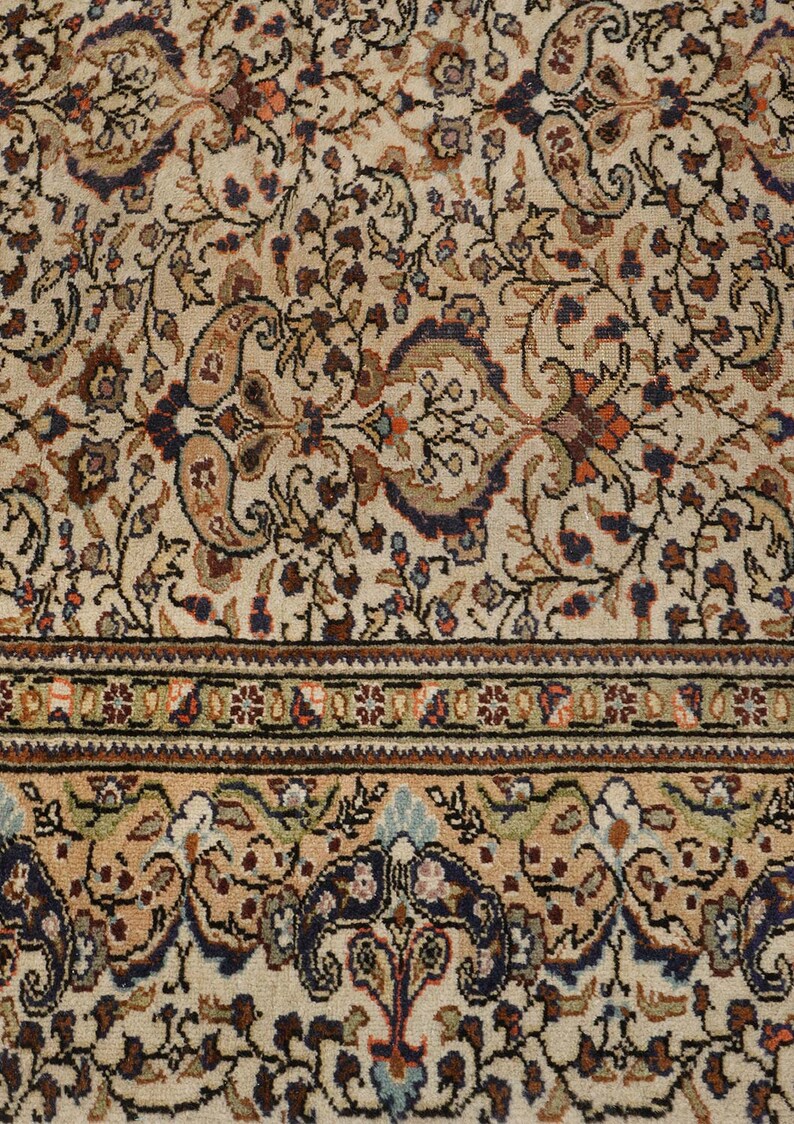 K&ouml;nnte beinhalten: Ein cremefarbener Teppich mit einem detaillierten Blumenmuster in Braun-, Blau- und Rott&ouml;nen. Der Teppich hat einen Rand mit einem sich wiederholenden Muster aus kleinen Quadraten.