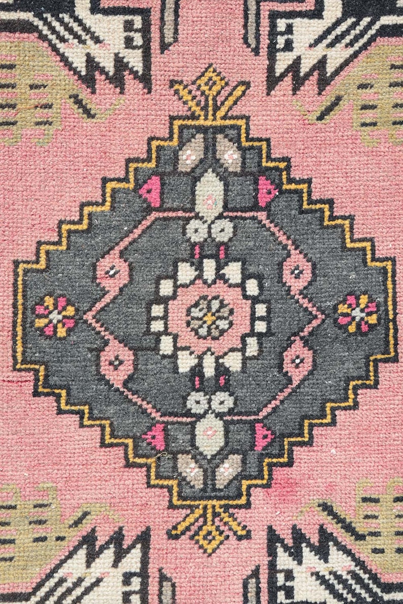 Pode incluir: Um tapete rosa com um design geom&eacute;trico em preto e branco. O tapete tem um medalh&atilde;o central com um padr&atilde;o floral.