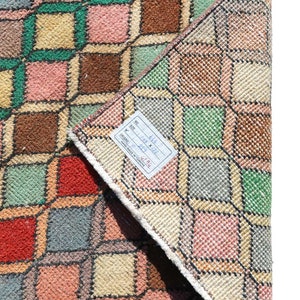 May include: A vintage Turkish rug with a geometric pattern in shades of pink, green, brown, and beige. The rug is folded in half and has a label attached to it that reads "No. 4118 Size: 1.88 x 2.22 M Origin: Turkey Hand Made in Turkey".
