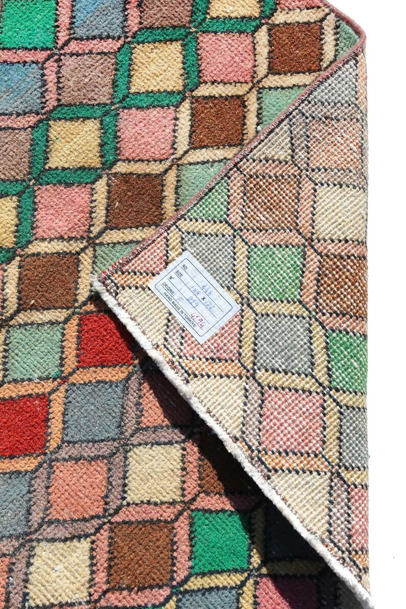 May include: A vintage Turkish rug with a geometric pattern in shades of pink, green, brown, and beige. The rug is folded in half and has a label attached to it that reads "No. 4118 Size: 1.88 x 2.22 M Origin: Turkey Hand Made in Turkey".