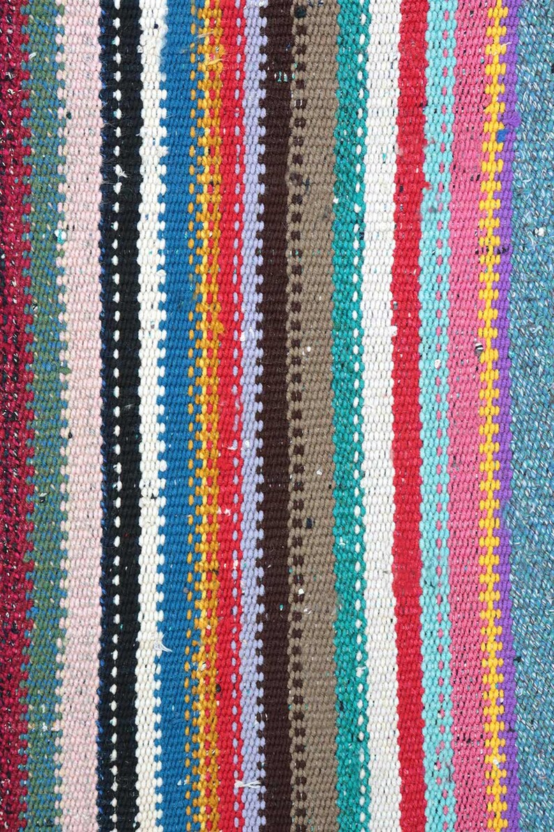 May include: A close-up of a colorful woven rug with stripes of pink, red, blue, green, yellow, and white.