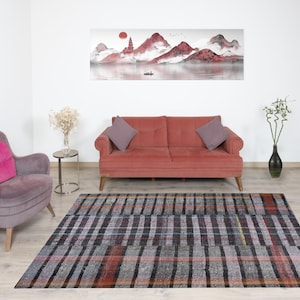 Könnte beinhalten: Ein rotes Sofa mit zwei Kissen und ein grauer Sessel mit einem rosa Kissen. Das Sofa und der Sessel stehen vor einem grauen und schwarzen gemusterten Teppich. Ein Gemälde einer Berglandschaft hängt an der Wand hinter dem Sofa.