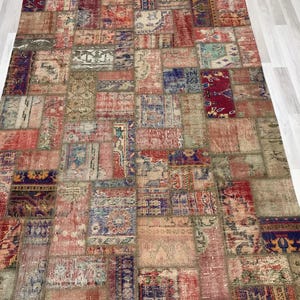 Puede incluir: Una alfombra rectangular de patchwork con una variedad de colores y patrones. La alfombra est&aacute; compuesta por numerosos parches rectangulares y cuadrados en tonos de rojo, azul, beige y verde. El dise&ntilde;o incluye motivos florales y geom&eacute;tricos.