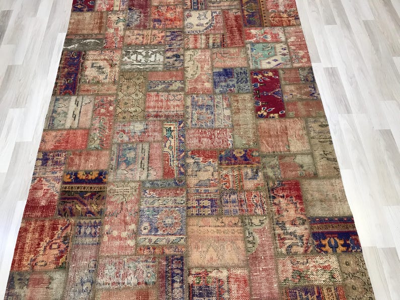 Puede incluir: Una alfombra rectangular de patchwork con una variedad de colores y patrones. La alfombra est&aacute; compuesta por numerosos parches rectangulares y cuadrados en tonos de rojo, azul, beige y verde. El dise&ntilde;o incluye motivos florales y geom&eacute;tricos.