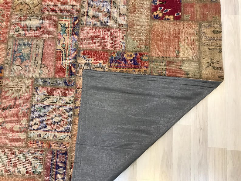 Puede incluir: Una alfombra patchwork con un aspecto envejecido y vintage. La alfombra presenta una variedad de parches rectangulares y cuadrados en tonos de rojo, beige, azul y naranja. La parte trasera de la alfombra es de tela gris lisa.