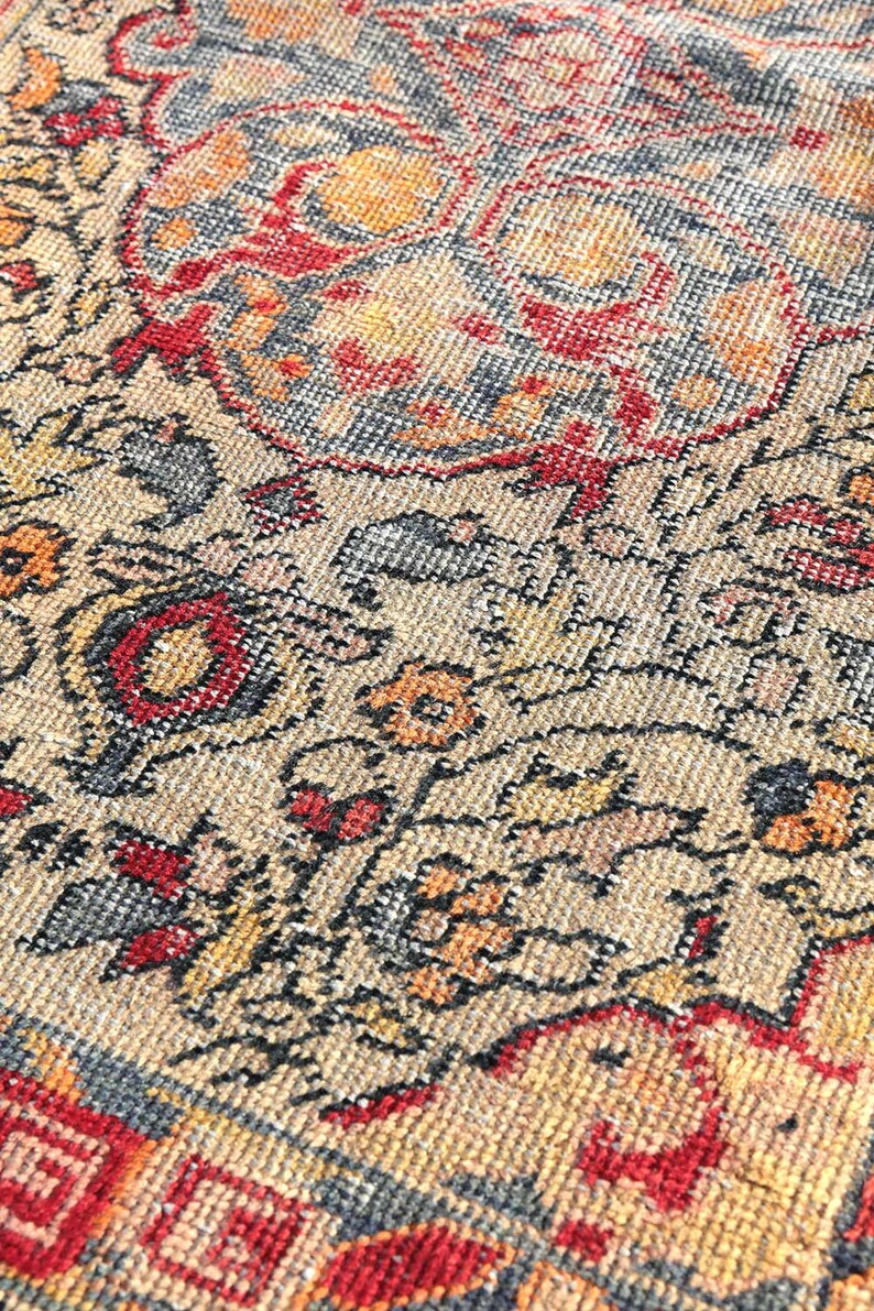 May include: Close-up of a beige rug with a detailed floral pattern in shades of red, orange, yellow, and black. The rug has a woven texture and a fringe border.