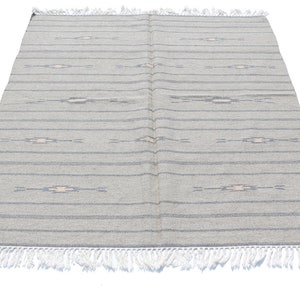 Puede incluir: Una alfombra rayada gris y blanca con un sutil patrón geométrico. La alfombra tiene un borde de flecos.