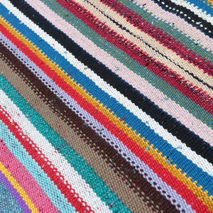 May include: A colorful striped rug with a variety of colors including red, blue, yellow, green, and white. The rug is woven with a thick, textured yarn.