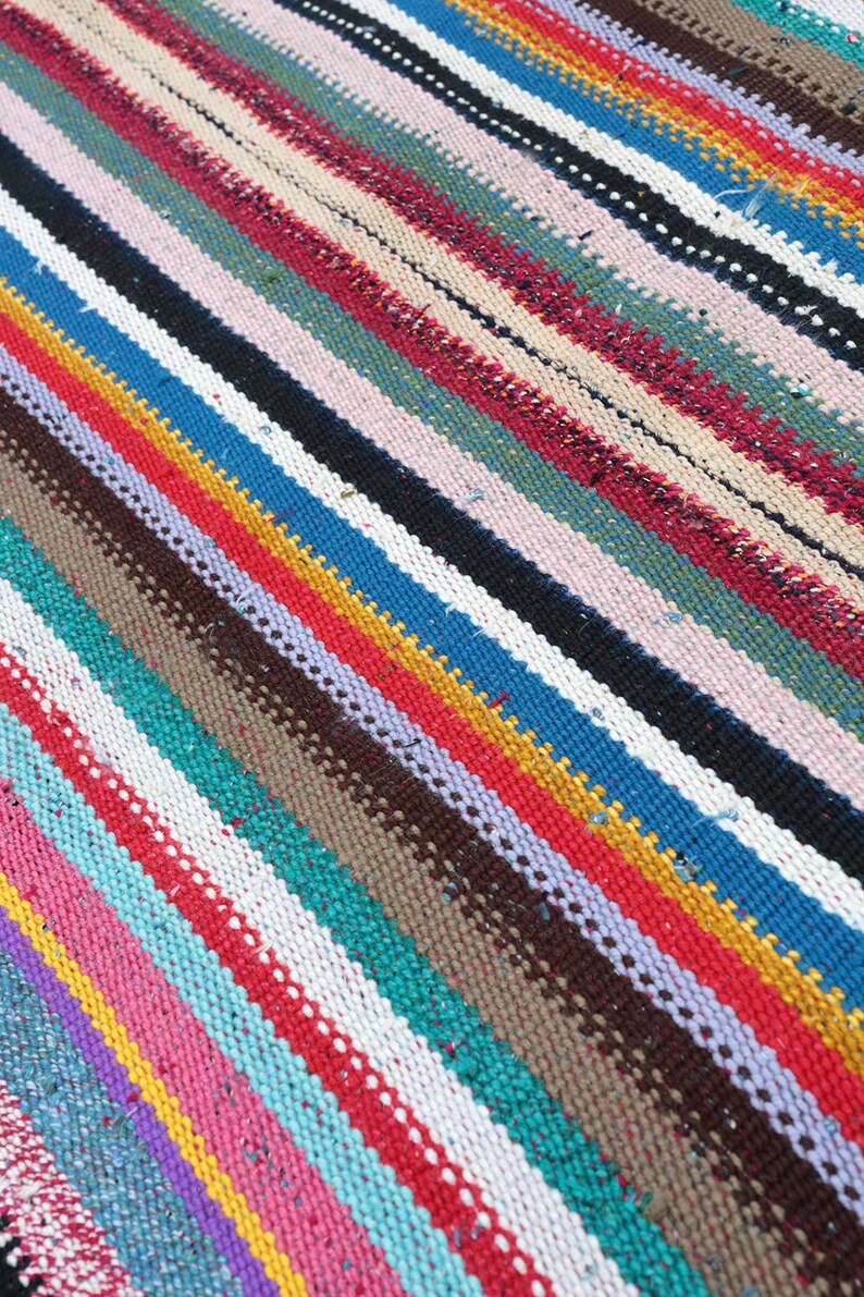 May include: A colorful striped rug with a variety of colors including red, blue, yellow, green, and white. The rug is woven with a thick, textured yarn.