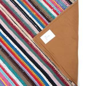 May include: Multicolored striped rug with a brown backing. The rug is made of woven fabric and has a fringed edge. The tag on the rug reads "85% 201 x 80 E".