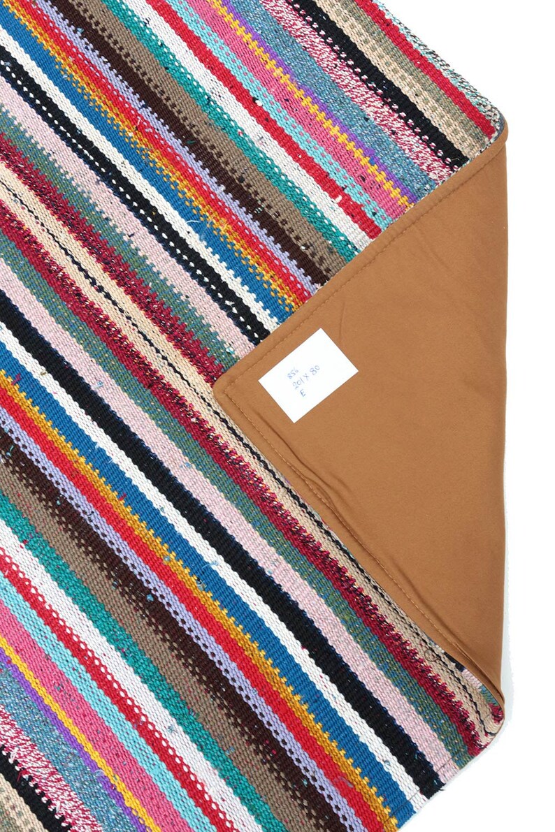 May include: Multicolored striped rug with a brown backing. The rug is made of woven fabric and has a fringed edge. The tag on the rug reads "85% 201 x 80 E".