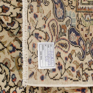 K&ouml;nnte beinhalten: Nahaufnahme eines beigen Teppichs mit Blumenmuster. Der Teppich hat ein Etikett mit der Aufschrift "NO. 5-R-H-132, SIZE: 288x207, 596 M&sup2;, ORIGIN: HAND MADE".