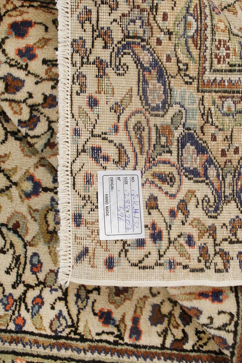 K&ouml;nnte beinhalten: Nahaufnahme eines beigen Teppichs mit Blumenmuster. Der Teppich hat ein Etikett mit der Aufschrift "NO. 5-R-H-132, SIZE: 288x207, 596 M&sup2;, ORIGIN: HAND MADE".