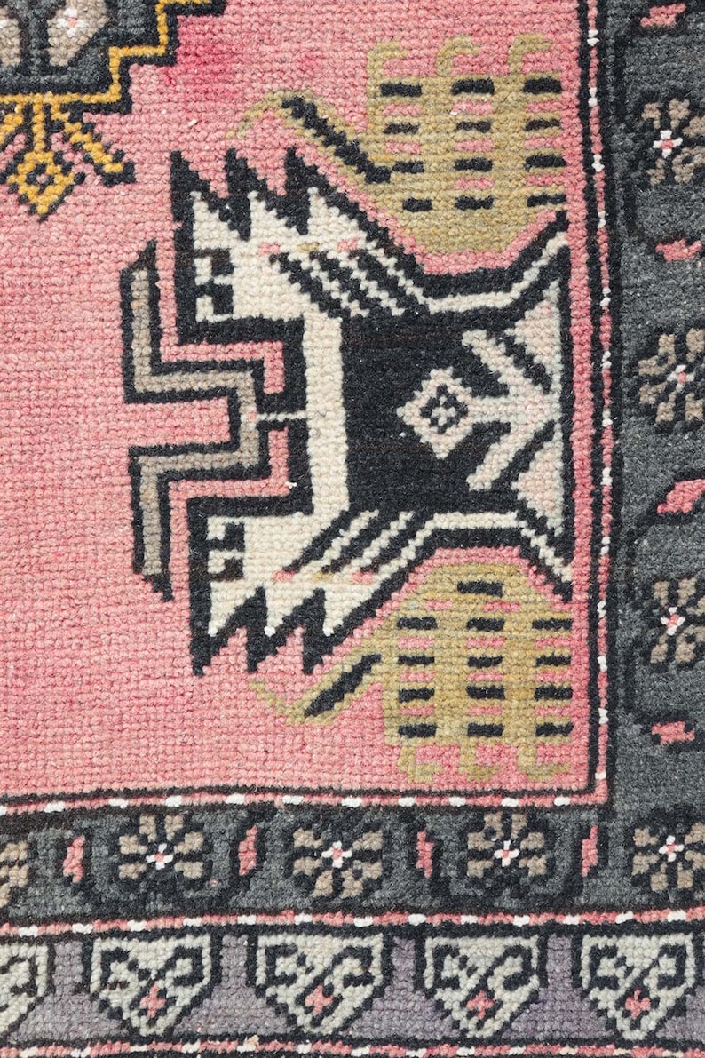 Pode incluir: Close-up de um tapete rosa e preto com um design geom&eacute;trico. O tapete tem uma borda de franja e &eacute; feito de l&atilde;.