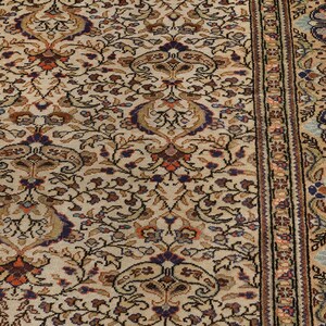 K&ouml;nnte beinhalten: Ein beiger Teppich mit einem detaillierten floralen Muster in Braun-, Blau- und Rott&ouml;nen. Der Teppich hat einen Rand mit einem sich wiederholenden geometrischen Muster.