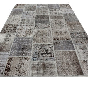 Puede incluir: Una alfombra de patchwork gris y marrón con una variedad de patrones. La alfombra está hecha de materiales reciclados y tiene un aspecto desgastado.