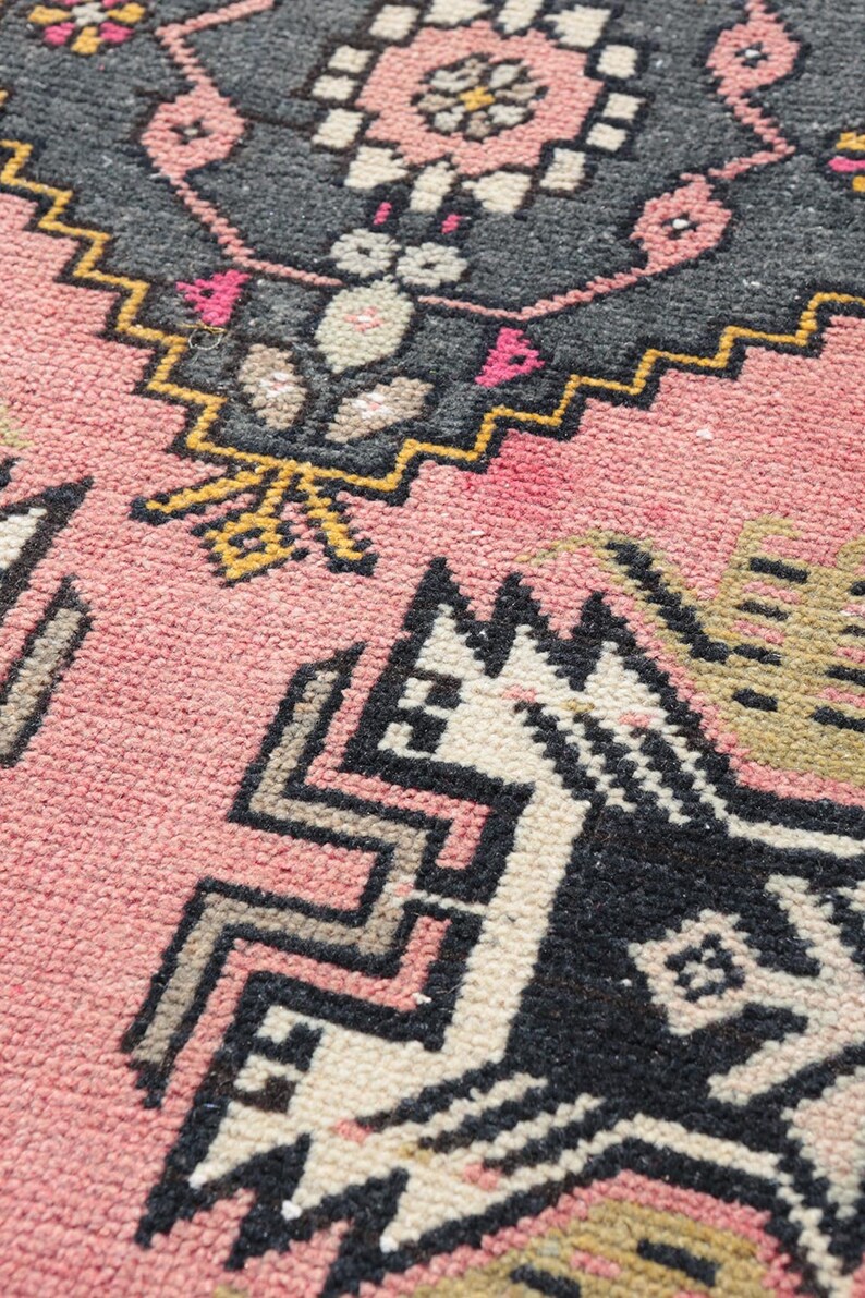 Pode incluir: Um tapete rosa com um padr&atilde;o geom&eacute;trico em preto, branco e amarelo. O padr&atilde;o apresenta um design de animal estilizado.
