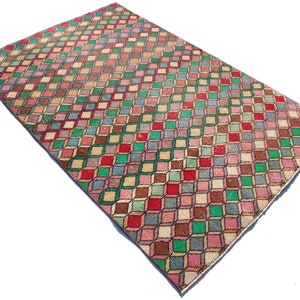 May include: A vintage rug with a geometric pattern of colorful squares in shades of pink, green, brown, and red. The squares are arranged in a diagonal pattern, creating a 3D effect.