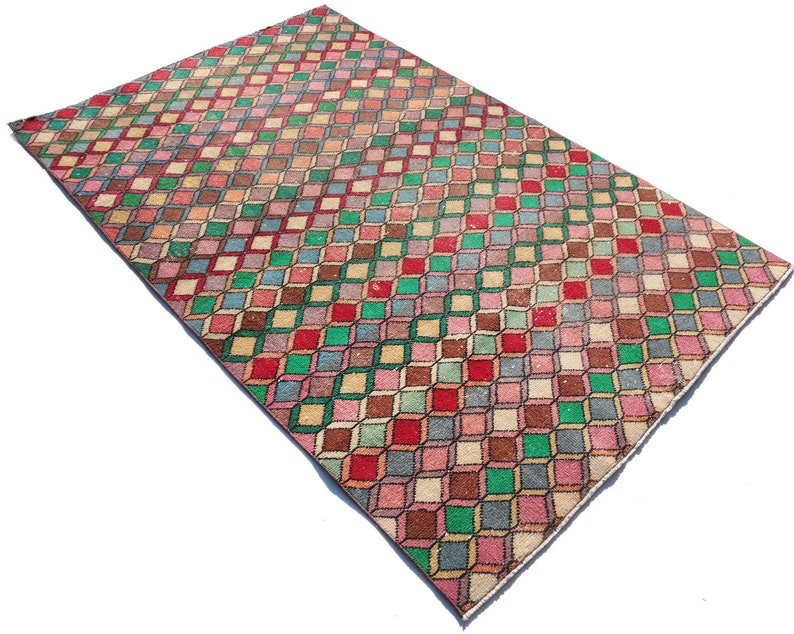 May include: A vintage rug with a geometric pattern of colorful squares in shades of pink, green, brown, and red. The squares are arranged in a diagonal pattern, creating a 3D effect.