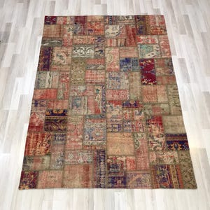Puede incluir: Alfombra rectangular de patchwork con aspecto envejecido. Presenta varios parches rectangulares y cuadrados en tonos rojos, azules, beige y marrones. Se encuentra sobre un suelo de madera clara.