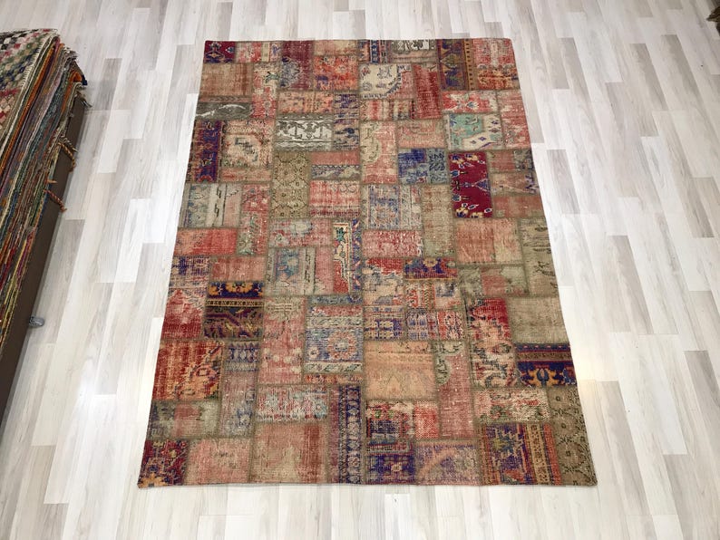 Puede incluir: Alfombra rectangular de patchwork con aspecto envejecido. Presenta varios parches rectangulares y cuadrados en tonos rojos, azules, beige y marrones. Se encuentra sobre un suelo de madera clara.