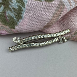 May include: A silver tone brooch with two rows of clear square rhinestones set in a curved design.